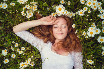 Beautiful young girl with curly red hair in camomile field