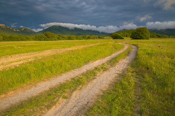 Fototapeta na wymiar Rural road to the mountains and the storm sky
