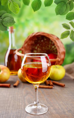 Apple cider in glass with cinnamon sticks and fresh apples on wooden table on natural background