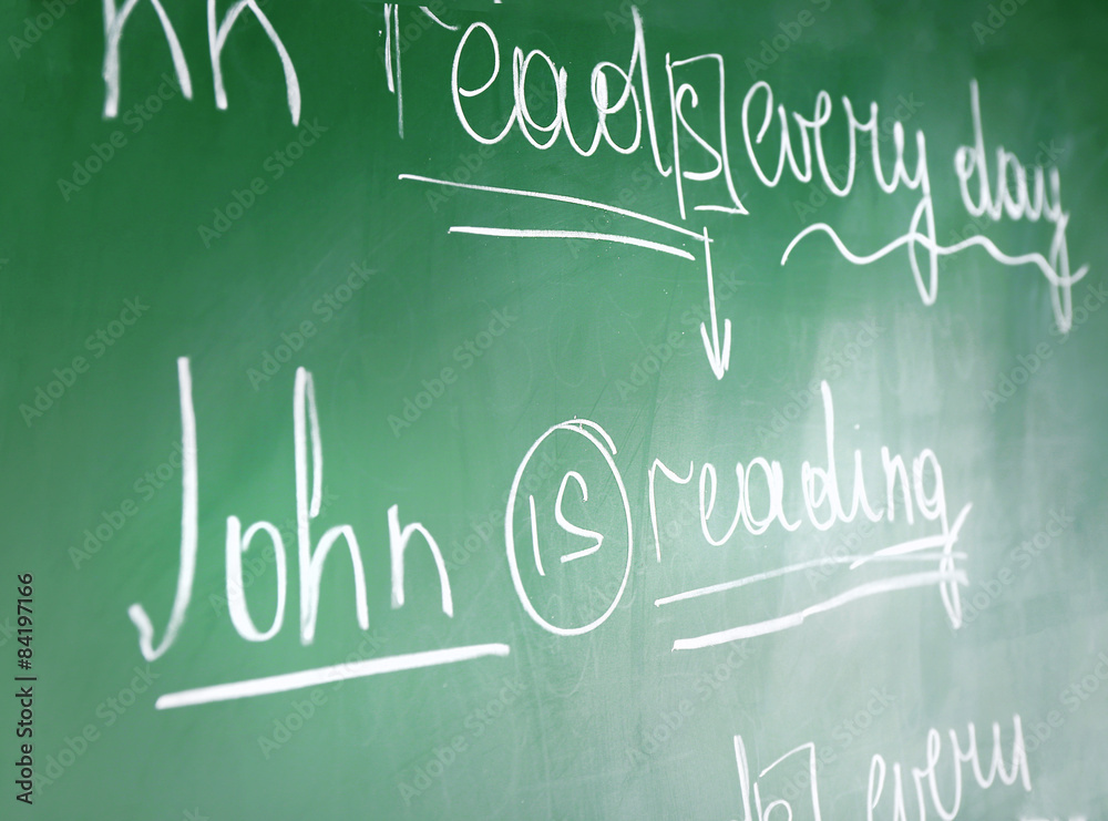 Wall mural Teacher hand writing grammar sentences on blackboard background