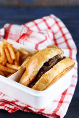 Tasty burger and french fries on plate, on wooden table background. Unhealthy food concept