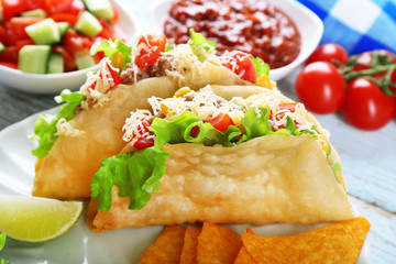 Tasty taco with nachos chips and vegetables on plate on table close up