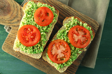 Vegan sandwich with avocado and vegetables on cutting board, on wooden background