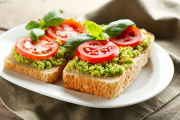 Vegan sandwich with avocado and vegetables on plate, on wooden background
