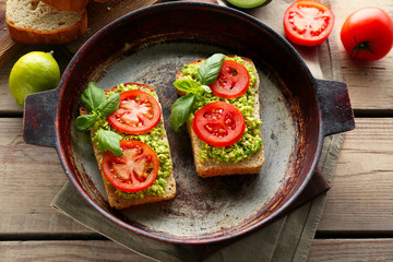 Vegan sandwich with avocado and vegetables on pan, on wooden background
