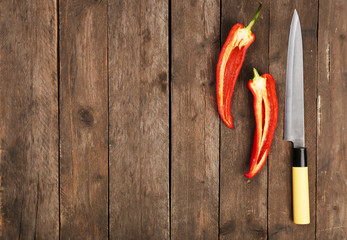 Halves of pepper chili with knife on wooden background