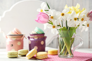 Spring bouquet in glass mug  and tasty macaroons on color wooden background