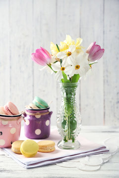Spring bouquet in vase and tasty macaroons on color wooden background