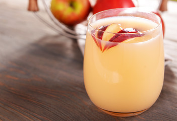 Glass of apple cider with fruits on wooden background