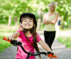 Naklejka premium Portrait of a little girl riding her bike ahead of her mother