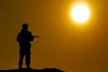 Fototapeta na wymiar Silhouette shot of soldier holding gun with colorful sky and mou