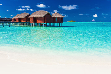 Overwater bungalow and beach in blue lagoon of tropical Maldives