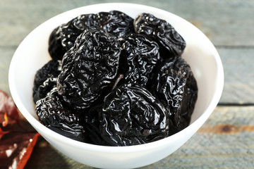 Saucer of prunes with leaves on wooden table, closeup