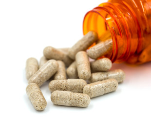 Herb capsules spilling out of a bottle.