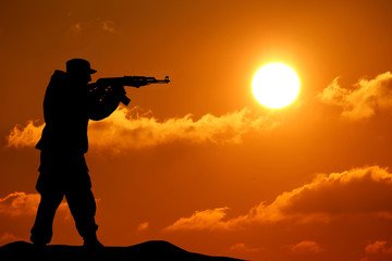 Silhouette shot of soldier holding gun with colorful sky and mou