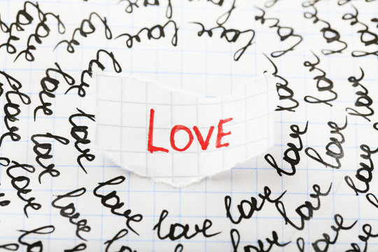 Word LOVE written on torn paper on sheet of paper background