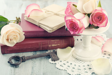 Fresh roses with old book and letters on color wooden table background. Vintage concept