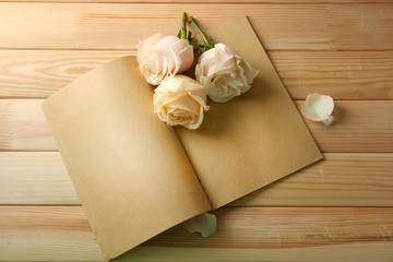 Fresh roses on old notebook, on wooden table background