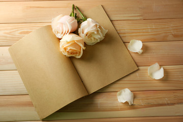 Fresh roses on old notebook, on wooden table background