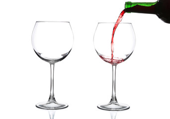 Red wine pouring from bottle into big glass on white background