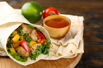 Homemade tasty burrito with vegetables on cutting board, on wooden background
