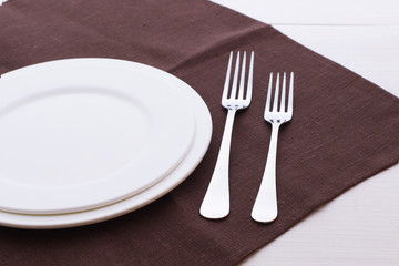 Empty plates and cutlery tablecloth on wooden table for dinner.