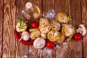 Pasta (tagliatelle) and flour on wooden surface.