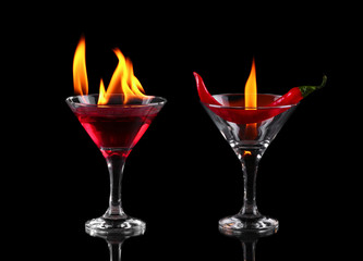 Hot chili pepper in a martini glass with a fire on a black backg