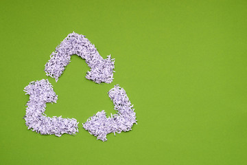 recycle symbol made from heap of shredded white paper on green