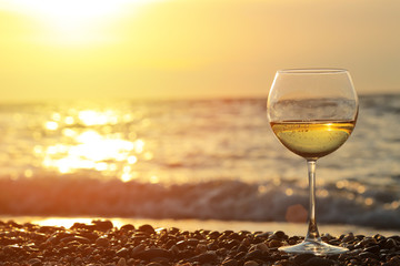 Verre de vin romantique assis sur la plage au coucher du soleil coloré