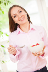 Smiling woman is having corn flakes with berries for breakfast