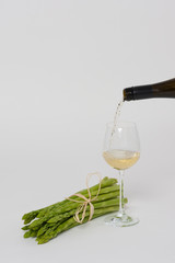 Grüner Spargel vor Weiss, Wein wird in ein Glas eingeschenkt