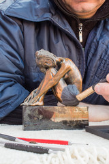 Hands of sculptor hold copper sculpture and clean it with brush