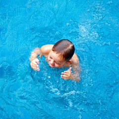 Fototapeta na wymiar cute kid, boy dabbling in pool water, top view