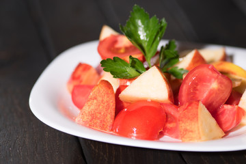 Salad tomato and apples in a bowl on a dark table. Vegan diet.