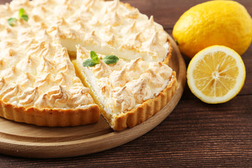 Lemon meringue pie on cutting board on wooden background