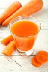 Glass of carrot juice on white wooden background