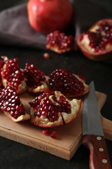 Delicious pomegranate fruit on cutting board on black background