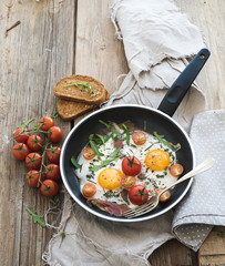 Pan of fried eggs, bacon and cherry-tomatoes with bread on