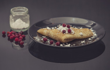 The pancakes are served on a black plate on a black background.