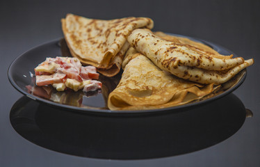 The pancakes are served on a black plate on a black background.