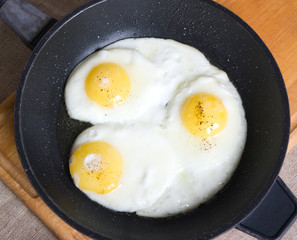 A pan with three fried chicken eggs on a wooden board
