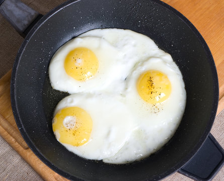 A pan with three fried chicken eggs on a wooden board