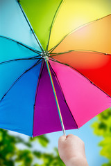 Rainbow umbrella in woman hands on nature background