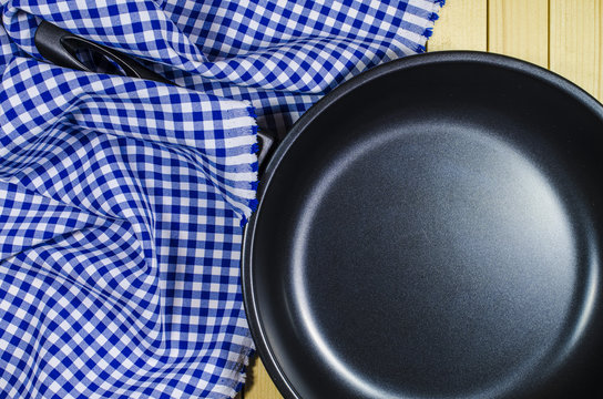 Folded tablecloth and frying pan on wooden background
