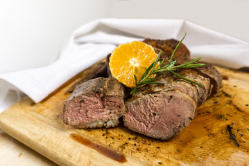 Slices of duck breast with rosemary and slice of orange on board