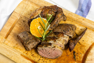 Slices of duck breast with rosemary and slice of orange on board