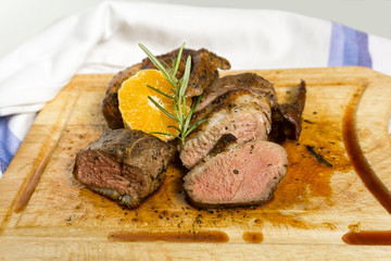 Slices of duck breast with rosemary and slice of orange on board