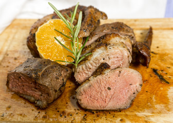 Slices of duck breast with rosemary and slice of orange on board