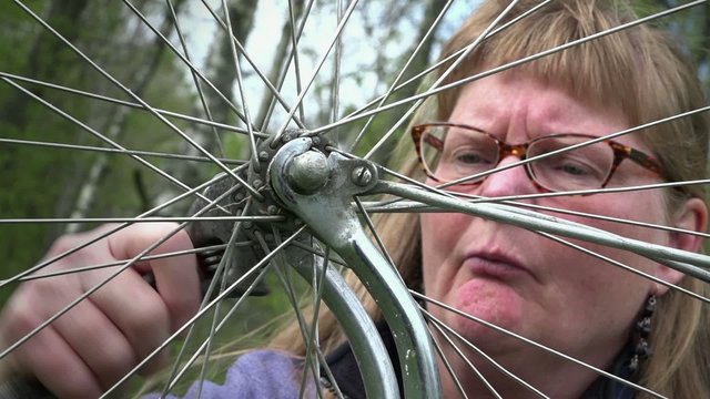 Woman is mending an old bike outdoors.
